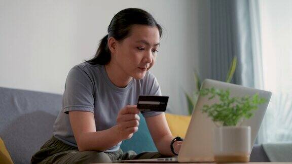 亚洲女性手持信用卡用笔记本电脑在家里的客厅里网上购物