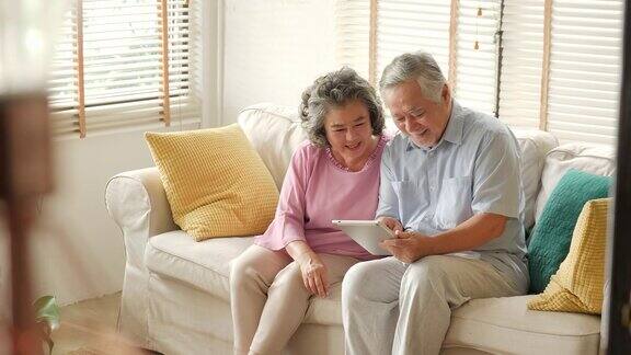 一对亚洲老年夫妇坐在家里的沙发上用着数字平板电脑聊天、微笑有科技观念的人