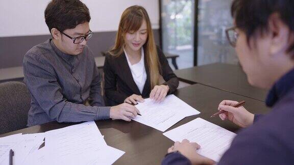 年轻的亚洲夫妇在男律师的办公室与他一起审阅、填写信息并在签署服务协议之前进行认真的讨论