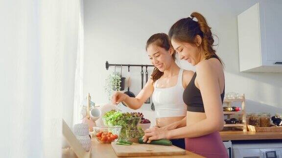 亚洲年轻的两个女子兄妹在厨房里穿着运动服烹饪沙拉活泼漂亮的女孩妹妹心情愉快喜欢吃蔬菜健康饮食减肥保健在家里