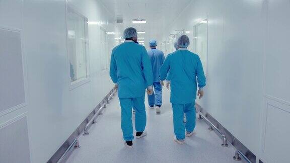 配戴防护口罩、身着防护服的医护人员在制药厂走廊内走动、交谈的背影