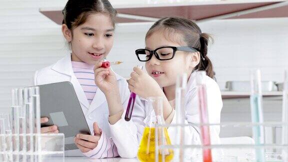 穿着白色长裙的可爱的小学女生在记事本上专心地做实验和记录现代技术教育孩子们在实验室的实验课上用玻璃管学习化学液体测试