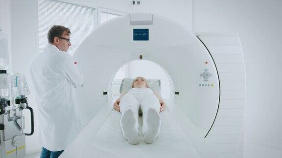 在医学实验室男性放射学家控制MRI或CT或PET扫描与女性病人进行程序医生使用先进的医疗技术进行紧急扫描