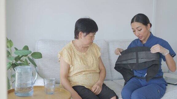 家庭护理人员在家访期间为亚洲老年妇女放回支撑带
