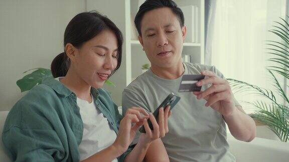 幸福的亚洲夫妇一起坐在家里客厅的沙发上用智能手机购物用信用卡在线支付生活方式花时间在家里