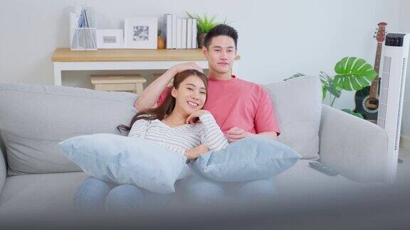 亚洲年轻情侣在家里的客厅一起看电影迷人浪漫的新婚男女坐在沙发上看电视节目在家里一起笑