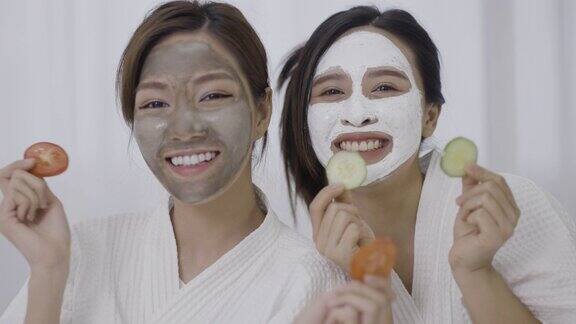 两名年轻女子脸上敷着面膜手里拿着番茄和黄瓜片
