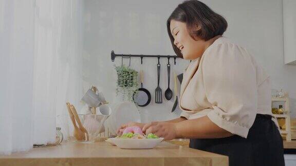 亚洲年轻的胖女人为盘子里的不健康食物感到高兴迷人的大码女孩走进厨房渴望选择甜甜甜圈而不是蔬菜沙拉在家里的桌子上