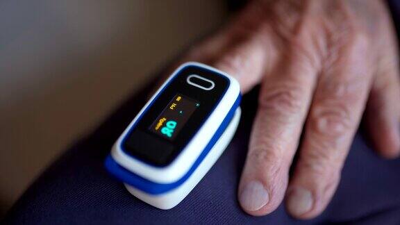 老年人手指上的数字脉搏血氧计的特写医疗监测装置闪烁并显示血氧饱和度水平老年人控制血氧率期间