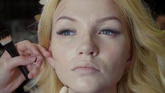 年轻的化妆师在模特脸上涂抹遮瑕膏