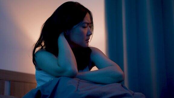 亚洲女人感到悲伤坐在床上抱着膝盖思考问题