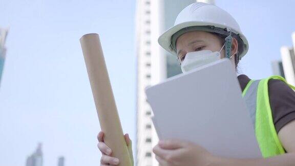 女性土木工程师或建筑设计师在城市建设工地的房地产建设项目中为了防止新冠肺炎的传播要戴安全帽、安全背心和口罩检查片上结构的渐进性