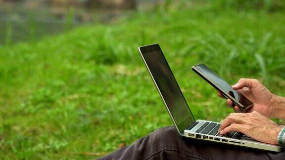 亚洲男子在公园露营度假时使用手机和笔记本电脑