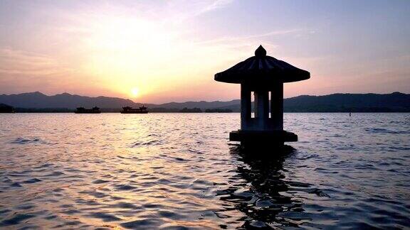 中国杭州西湖美丽的夕阳景观橘色的黄昏天空和宁静的水与湖中的传统亭台楼阁闪烁的涟漪4k电影慢镜头