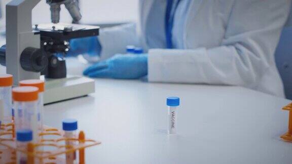 近距离观察实验室工作人员使用显微镜进行研究持有标有疫苗的试管