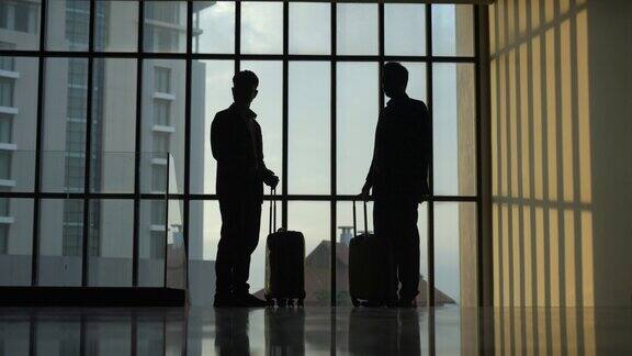 一个商人和一个女商人的剪影带着行李箱走在一个有大窗户的大办公室里