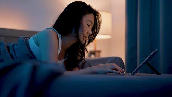 亚洲女性晚上在卧室里玩平板电脑