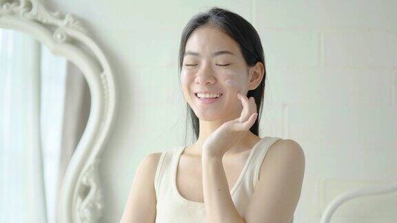 慢动作肖像年轻的亚洲妇女使用面霜在她的脸上概念为新鲜滋润肌肤美丽近距离美容脸快乐健康模式年轻的黑发女孩照顾她的皮肤