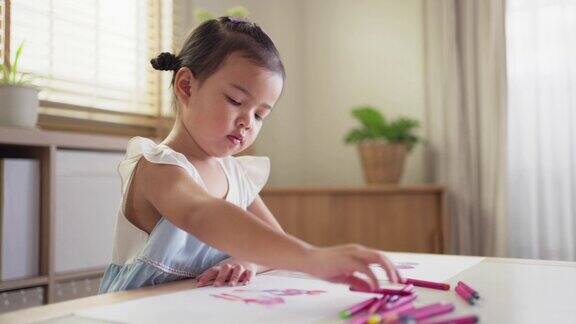 顽皮可爱的亚洲小女孩喜欢在家里的客厅用彩色蜡笔在纸上画画和着色孩子的技能发展和创造性活动在家学习艺术在周末