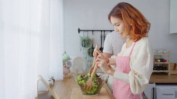 亚洲美女和丈夫在家里厨房做蔬菜沙拉年轻漂亮的情侣心情愉快喜欢吃蔬菜健康饮食减肥在家保健