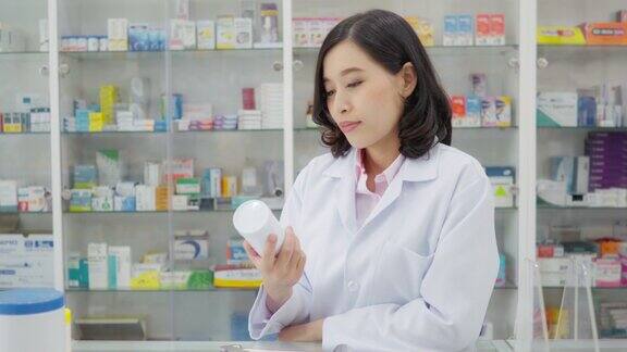 在药店背景的亚洲药剂师的英雄肖像医疗保健和医疗概念药店药剂师微笑着拿着药瓶向顾客建议如何使用药片