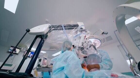 手术室的神经外科手术外科医生和助手通过现代显微镜进行神经外科手术