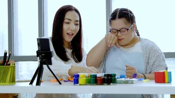 亚洲母亲和自闭症女儿学习练习橡皮泥和绘画在家通过智能手机在线学习意图快乐母亲节概念