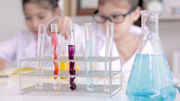 小学生穿着白大褂在学校实验室学习化学在科学课上一边做化学实验一边分析和混合试管中的液体教育实验室概念