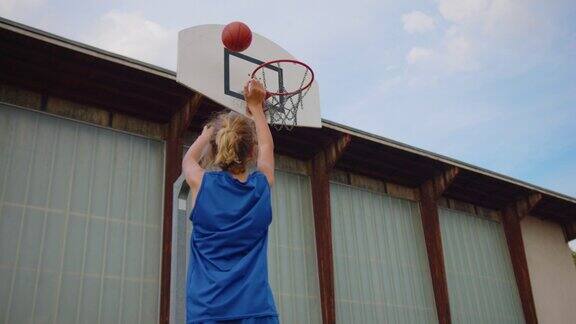 一个穿着蓝色篮球服的男孩在玩一个橙色的球在学校操场上进行篮球训练青少年在业余时间打篮球