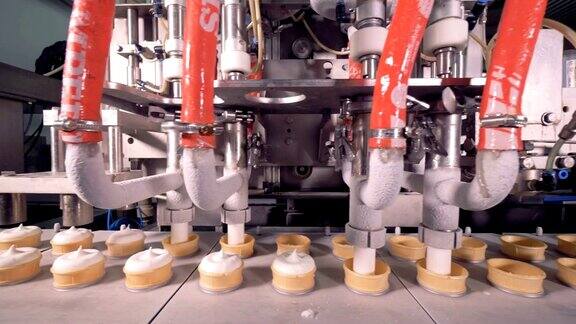 四个工业管正在向移动的威化杯中填充冰淇淋物质