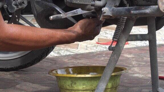 摩托车汽车机械师的手拧紧发动机缸体底部机油流出处的螺栓换机油
