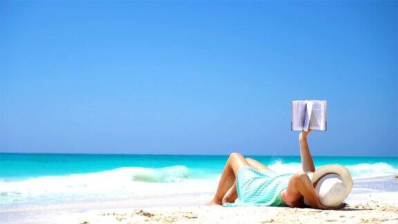 年轻女子在热带的白色沙滩上看书