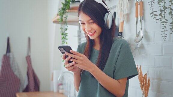 微笑的亚洲女人在家里的厨房用智能手机听音乐广播或播客科技生活方式