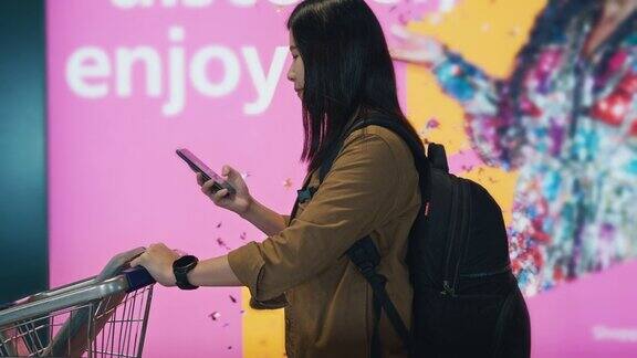 在机场门口的走道上亚洲女旅客边走边用手提行李车用手机