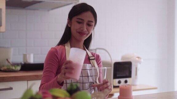 年轻的亚洲妇女在家里厨房的柜台上用搅拌机倒一杯健康的水果奶昔作为早餐