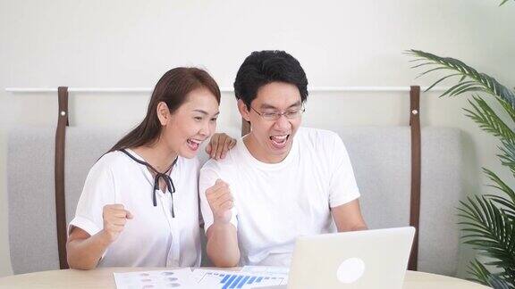 慢动作激动的亚洲夫妇使用笔记本电脑获奖者