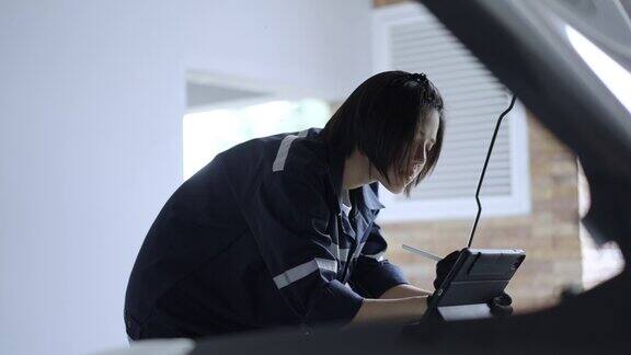 亚洲美女机械师在车库用数码平板电脑检查修理后的汽车状况