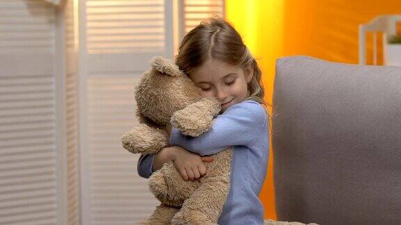 可爱的卷毛的学龄前女孩拥抱着泰迪熊微笑着快乐的童年