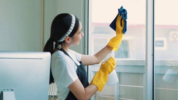 一个打扫房子的女人的特写镜头她一边打扫桌子一边用喷雾器和蓝色布擦灰尘房屋清洁概念