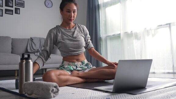 运动的亚洲年轻女性在家锻炼在互联网上观看健身视频或在线健身课程使用笔记本电脑客厅室内