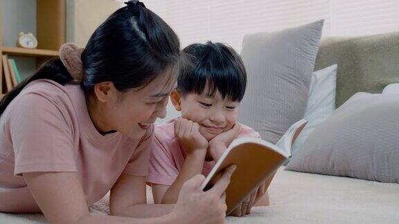 4K亚洲妈妈和男孩穿着粉红色的t恤他们两个舒服地躺在床上妈妈手里拿着一本剧本给儿子读他们两个玩得又温暖又可爱