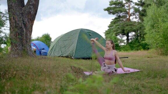棕色头发的女人在露营地的粉色垫子上练习瑜伽
