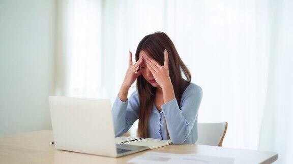 办公室综合症劳累过度的年轻亚洲女性在电脑工作后感到头痛和视力问题紧张的年轻女子在家里饱受疲劳之苦