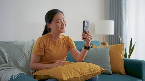 亚洲女性坐在家里客厅的沙发上用智能手机打视频电话