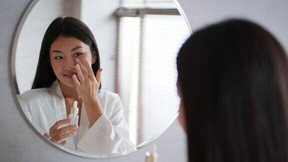快乐的韩国女士站在浴室里使用面部精华液