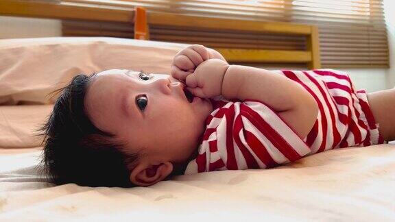 可爱的亚洲小男孩的肖像穿着红白条纹衬衫吮吸手指