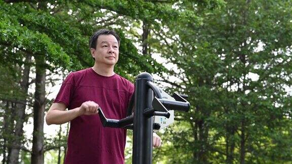 一位中年亚洲男子在公园用健身器材锻炼身体