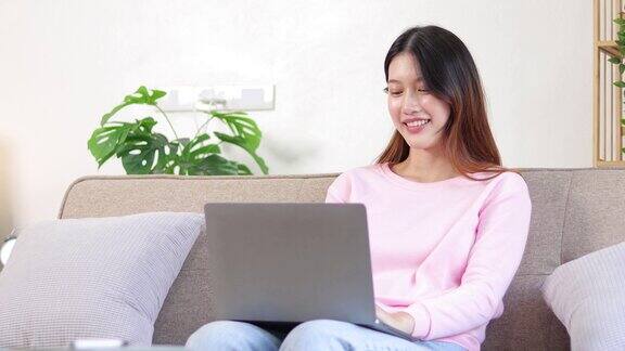 迷人的亚洲女子随意地使用笔记本电脑在家里的客厅放松