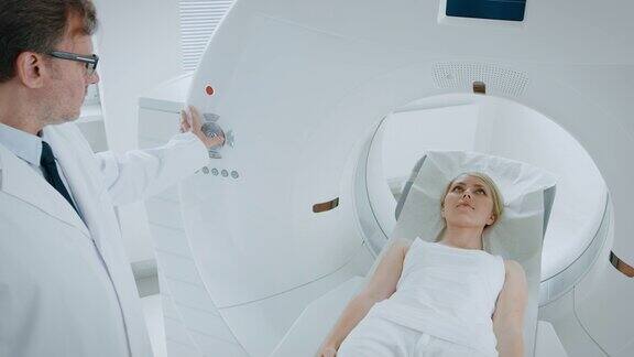 在医学实验室男性放射学家控制MRI或CT或PET扫描与女性病人进行程序高科技现代医疗设备提升相机拍摄