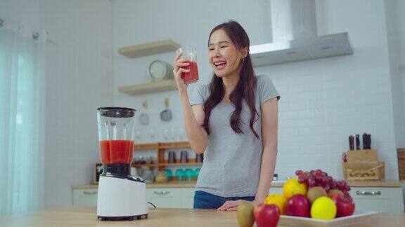 年轻的亚洲妇女在家厨房里做果汁她在家里笑着喝着饮料